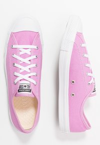 Baskets en toile rose avec semelles en caoutchouc blanc et lacets, dotées d'une étiquette noire "Converse All Star" et d'œillets métalliques circulaires.