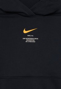 Crna dukserica s kapuljačom od mekog materijala, koja sadrži istaknutu narančastu Nike swoosh logotip i bijeli tekst s podacima o tvrtki.
