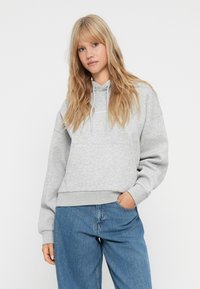 Felpa con cappuccio grigia chiara, con tasca frontale e orlo a coste. Indossata con jeans in denim blue dalla vestibilità ampia. Tessuto morbido.