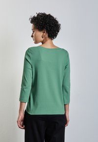 Top vert à côtes avec un large col et des manches trois-quarts, associé à un pantalon noir ample. Tissu texturé avec une coupe décontractée.