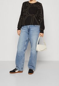 Svart långärmad topp med gula streck, ljusblå vida jeans, svarta sneakers med vita och beige detaljer, samt en vit handväska.