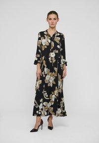 Garš melns puķains kleita ar apkakli, ar baltām un b ēšām ziediem. Volānu piedurknes un gluda tekstūra. Kopā ar melniem augstpapēžu kurpēm.