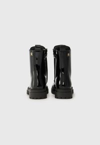 Sorte patent ankle boots med en chunky såle, bageste trækstrop og guldhardware detaljer. Glat tekstur med et elegant, moderne design.