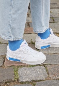 Vita sneakers med blå accenter, med perforerad design, gummisula och vadderad krage. Bärs med blå ribbade strumpor och avklippt denim.