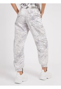 Pantalon cargo blanc et gris à motifs, avec poignets élastiques et poches latérales, associé à des baskets blanches. Note : design texturé évoquant des formes abstraites.