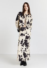 Donna che indossa una blusa corta con allacciatura anteriore a pois crema e nera, abbinata a una gonna lunga coordinata e stivaletti neri, su uno sfondo bianco semplice.