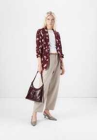 Blazer floreale bordeaux su top bianco, pantaloni beige a gamba larga, scarpe con tacco grigie, borsa in pelle bordeaux con dettaglio a fibbia, sfondo uniforme.