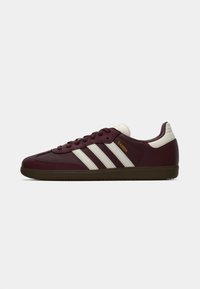 Marron lædersneakers med hvide striber og en tekstureret gummisål. Har en polstret krave og guld "Samba" branding på siden.