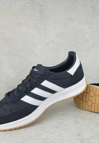 Sportske cipele s gornjim dijelom u sivoj boji, bijelim prugama i potplatom od gume. Imaju vezanje i podstavljeni ovratnik za udobnost.