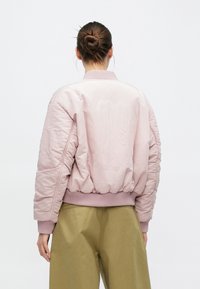 Giacca bomber rosa con finitura lucida, polsini e orlo a costine. Presenta un design testurizzato sulla schiena e una vestibilità comoda.