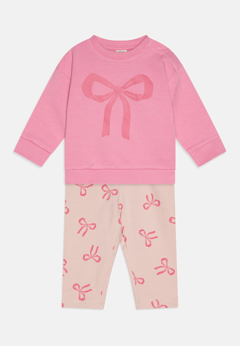 Rosa Sweatshirt mit einer großen Bogen-Grafik, kombiniert mit hellbeigen Leggings, die kleine rosa Bogenmuster aufweisen. Weicher Stoff, lässiges Design.