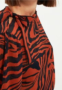 Punamusta raidallinen pusero, jossa on solmittava kaula-aukko. Väljä leikkaus ja kevyt, laskeutuva kangas.