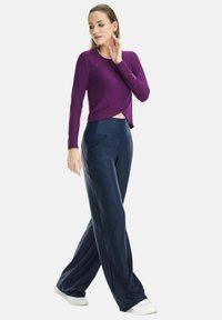 Purple long-sleeve top with a cropped front and rounded hem paired with loose navy pants featuring side pockets and a wide waistband.