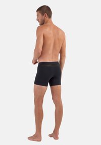 Schwarze Boxershorts aus dehnbarem Stoff, mit elastischem Bund und figurbetontem Design, von hinten betrachtet.