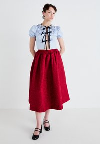 Cropped light blue blouse with puff sleeves and black accents, paired with a long red skirt featuring a subtle floral pattern and black shoes.