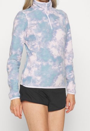 Femme portant un haut polaire bleu et blanc tie-dye à manches longues avec fermeture éclair et un short noir sur fond blanc.