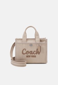 Beżowa torba płócienna z podwójnymi uchwytami, regulowanym paskiem na ramię oraz wyszywanym brązowym logo "Coach New York". Z elementami srebrnej biżuterii.