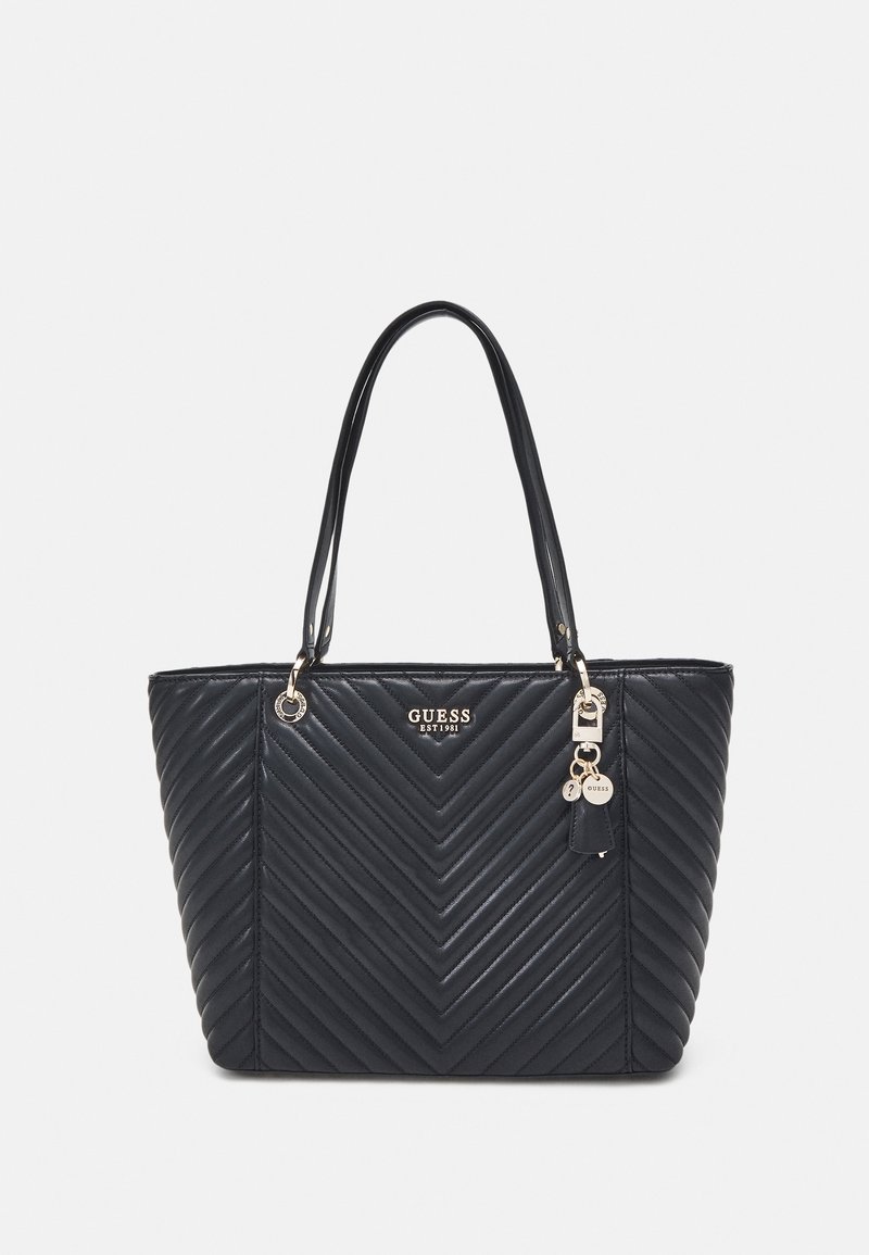 Sac cabas matelassé noir avec doubles anses, logo "Guess" doré et pendentifs suspendus sur le devant.