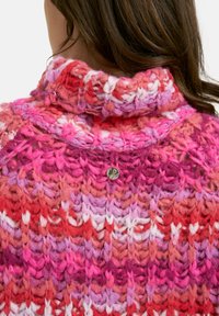 Strickpullover mit hohem Kragen, der einen Farbverlauf von Rosa- zu Rottönen zeigt, aus strukturiertem Garn gefertigt ist und ein kleines metallisches Logodetail auf dem Rücken hat.