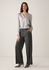 Hellgraue Bluse mit langem Arm und V-Ausschnitt, kombiniert mit grauen, strukturierten Hosen mit weitem Bein. Hohe Absatzschuhe komplettieren das Outfit.