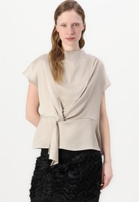 Beige top s krátkým rukávem a uzlovým detailem vepředu, s volným střihem. Vytvořený s černou sukní se sklady. Jemná textura látky.
