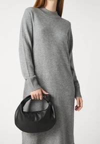 Abito grigio a maglia con polsini a costine, abbinato a una borsa in morbida pelle nera con manico annodato.