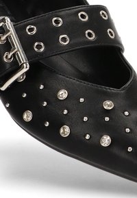 Zapato de cuero negro con un diseño recortado, adornado con tachuelas plateadas y una correa con hebilla. Textura suave y forma de punta afilada.