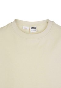 Krēmkrāsas Urban Classics t-krekls ar apaļu kakla izgriezumu un redzamām zīmēm, kurās norādīts izmērs un ugunsdrošības brīdinājums.