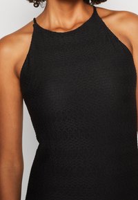 Robe noire à col licou en tissu texturé avec un motif côtelé. Le design présente une silhouette ajustée et une coupe sans manches.