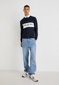 Námornícky polo s dlhým rukávom a bielym golierom, s veľkým logom "Pepe Jeans London". Svetlomodré voľné džínsy a šedé tenisky s akcentmi.