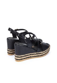 Sandales compensées noires avec dessus texturé, brides entrecroisées et plateforme en jute tressé. Détail de boucle sur la bride de cheville pour un accent.