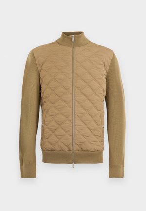 Veste matelassée beige avec manches, col et ourlet en tricot côtelé, dotée d'une fermeture éclair frontale et de poches latérales à pression.