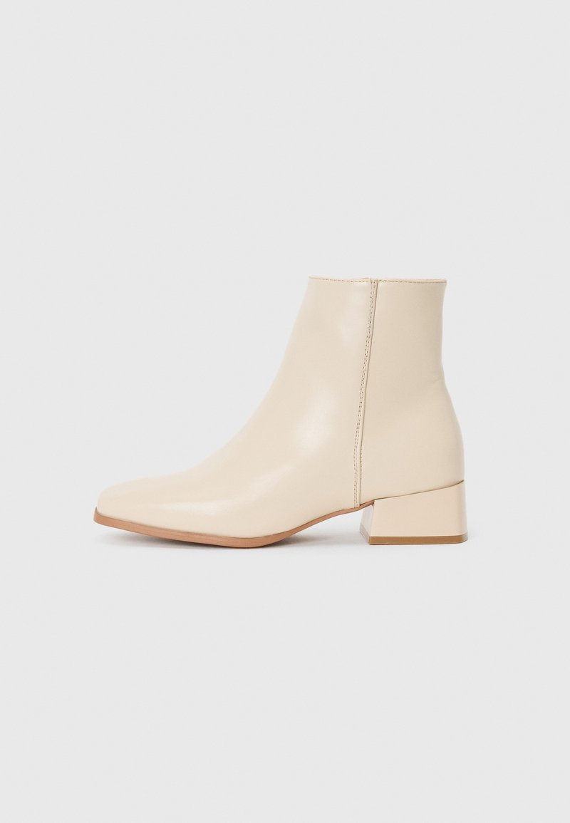 Bottine de couleur crème avec un petit talon bloc et une finition en cuir lisse, vue de profil sur un fond blanc uni.