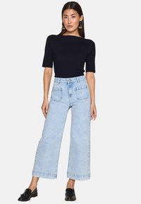 Top corto a maniche corte nero a righe abbinato a jeans a gamba larga di un blu chiaro e mocassini neri. Caratteristiche notevoli includono vita alta e tasche.