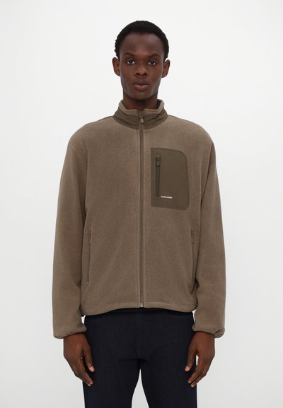 Braune Fleecejacke mit hohem Kragen, Reißverschluss vorne und einer Brusttasche auf der linken Seite. Sie zeichnet sich durch eine weiche Textur und ein dezentes Branding-Detail aus.