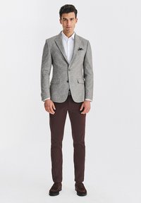 Szary blazer z klapkami i dwoma przednimi kieszeniami, zestawiony z białą koszulą i ciemnobrązowymi chinosami. Brązowe buty dopełniają stylizację.