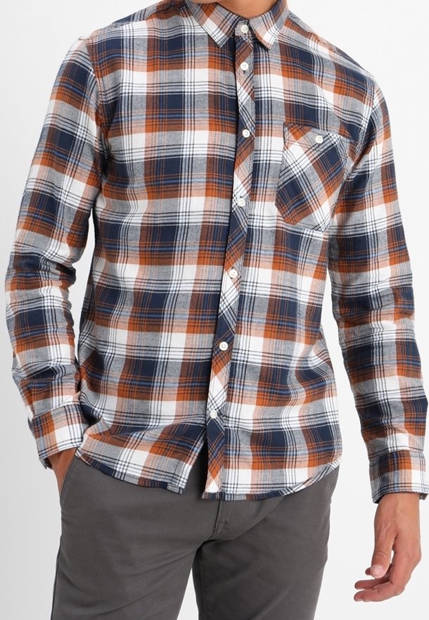 Homme portant une chemise à carreaux boutonnée à manches longues en blanc, bleu marine et orange avec une poche poitrine et un pantalon gris.