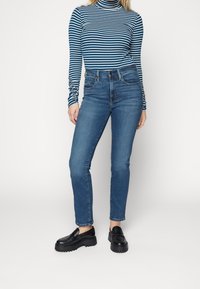 Modrý a bílý proužkovaný rolák ve spojení s úzkými, vysokým pasem tmavě modrými džínami. Modelka má na sobě černé platformové mokasíny.