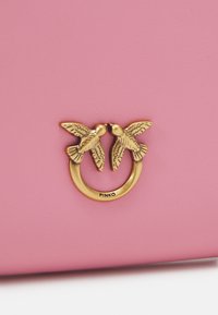 Borsa in pelle rosa con accessori in metallo dorato che presenta due motivi di uccelli. Texture liscia, design minimalista e nome del marchio "PINKO" ben visibile.