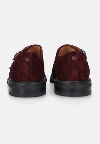 Burgunderfarbene Wildlederschuhe mit runder Zehenform, ausgestattet mit einer schwarzen Gummisohle und einem seitlichen Schnallenverschluss, der eine glatte Textur zeigt.