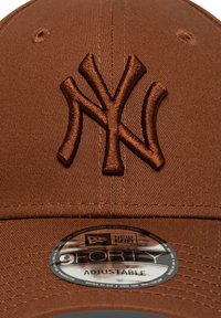 Brown cap featuring an embroidered NY logo in a darker brown. Includes an adjustable strap and a circular New Era tag on the brim.
