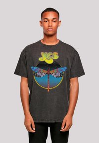 Black oversized graphic t-shirt featuring a multicolored dragonfly design with a circular background; cotton material, crew neck, short sleeves.