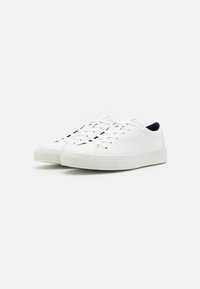 Sneakers bianchi in pelle con punta arrotondata, suola piatta e design minimalista. Chiusura con lacci che presenta piccoli fori di ventilazione.