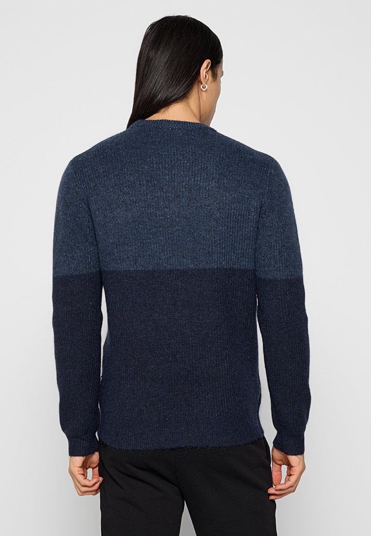Granatowy sweter z dzianiny z efektem kolorowych bloków; jaśniejsza niebieska górna część przechodzi w ciemniejszą granatową dolną część; struktura ribbed, długie rękawy.