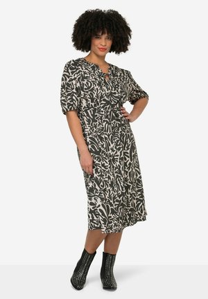 Knee-length dress in beige with a dark abstract pattern, featuring a keyhole neckline and puffed sleeves. Worn with black, studded ankle boots.