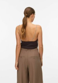 Bruine spaghetti-top met een lage rug, gecombineerd met hooglopende beige broeken met dubbele achterzakken en een getailleerde pasvorm.