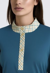 Blusa turchese con colletto beige e blu a motivo. Presenta una patta frontale con tre bottoni e una texture del tessuto morbida.