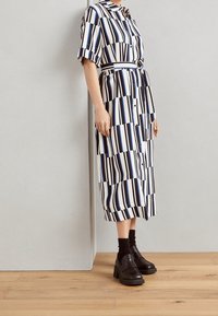 Abito camicia a righe nei colori nero, bianco e blu, con bottoni frontali, maniche corte e vita con cintura. Indossato con scarpe nere chunky.