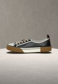 Ασπρόμαυρο sneaker χαμηλής κοπής με καφέ ριμπ λεπτομέρειες στη μύτη και τη φτέρνα, εκρού κορδόνια και διακοσμητικό σχέδιο στη λευκή μεσαία σόλα.