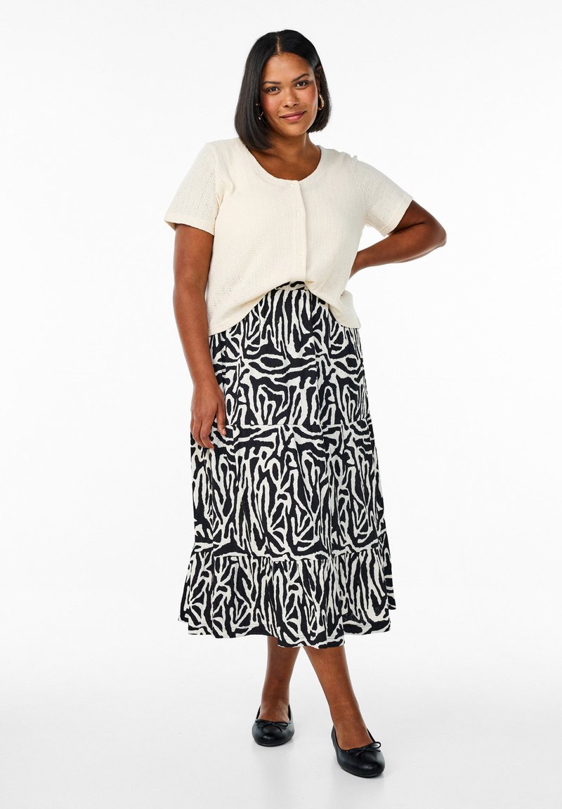 Haut tricot crème à manches courtes avec des boutons, assorti à une jupe à volants en imprimé animal noir et blanc. Porté avec des chaussures plates noires.